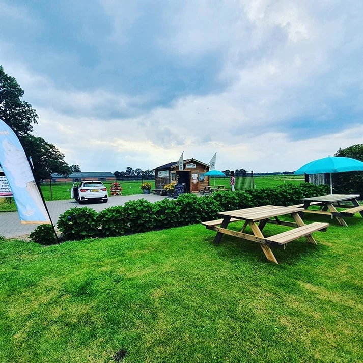Het terras van De Hugtenhoeve met picknicktafels, parasol en uitzicht over het erf