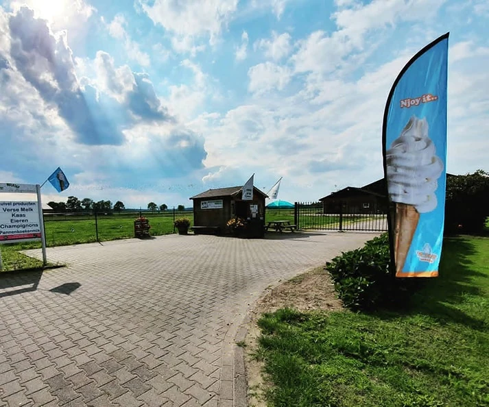Buitenterrein van Melktap De Hugtenhoeve met de boerderijwinkel en softijsvlag